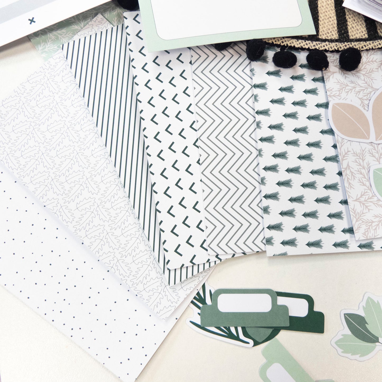 Paquets de papier décoratif à motifs modernes et géométriques verts et gris, avec étiquettes et pièces décoratives en dessous.