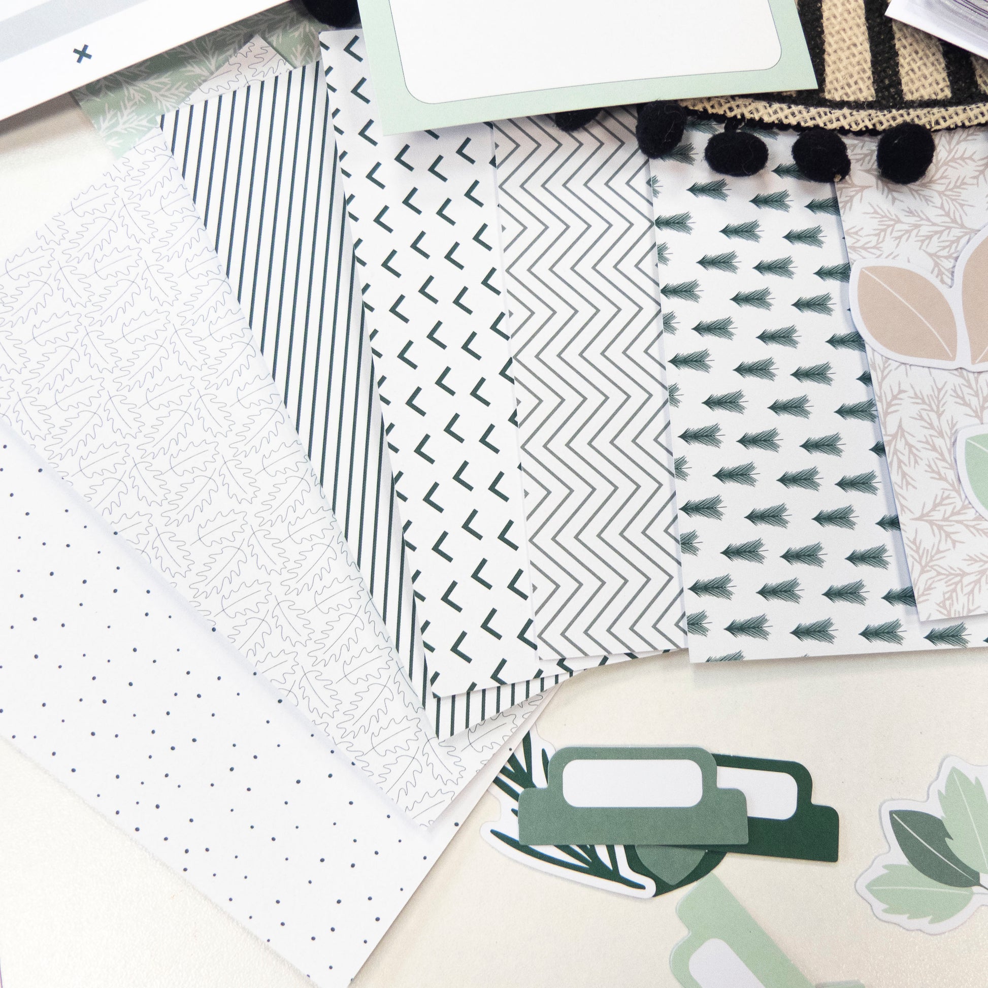 Paquets de papier décoratif à motifs modernes et géométriques verts et gris, avec étiquettes et pièces décoratives en dessous.